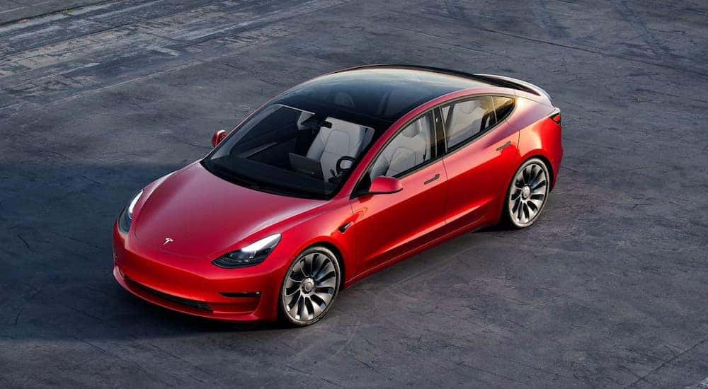 A red Tesla Model 3 is shown parked in an empty lot.