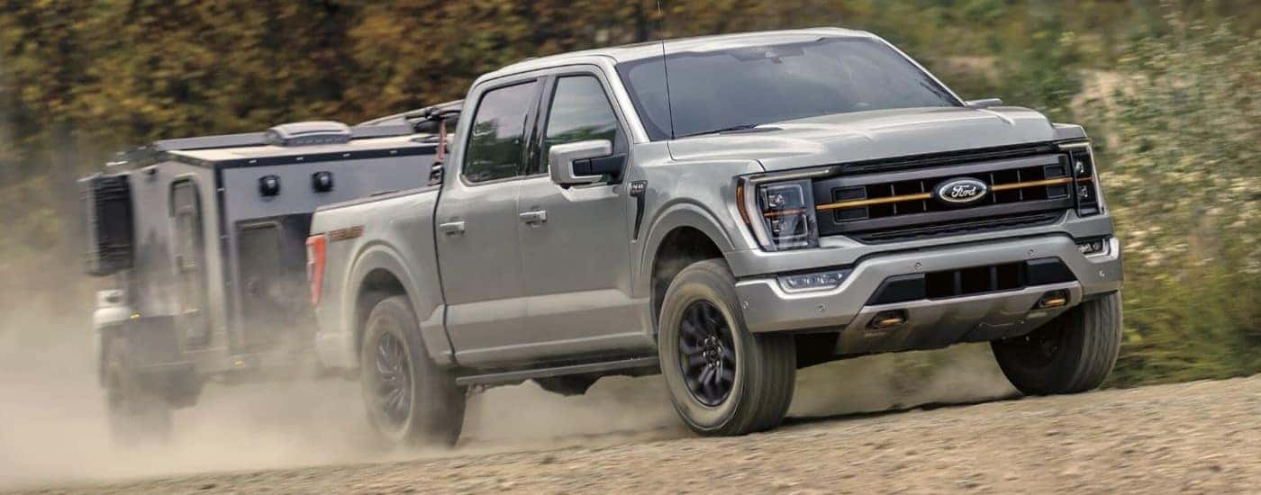 A grey 2023 Ford F-150 Tremor is shown towing a trailer on a dusty trail.