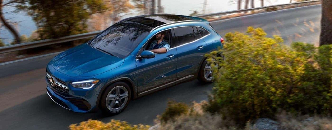 A blue 2022 Mercedes-Benz GLA 250 is shown driving past a lake after looking at cars for sale in Omaha.