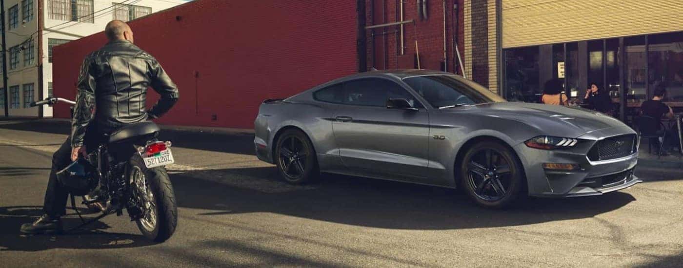 A dark grey 2021 Ford Mustang GT is shown on a street next to a motorcycle.