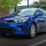 A blue 2023 Kia Rio is shown driving on a city street after viewing cars for sale in Hartford.