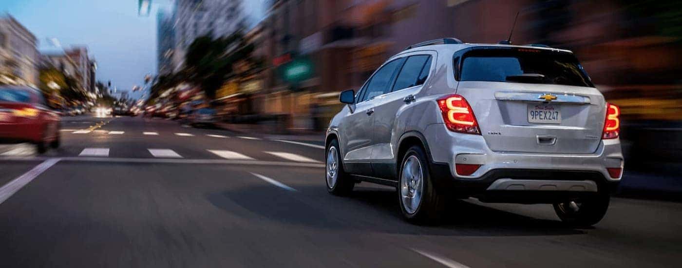A silver 2020 Chevy Trax is shown from a rear angle driving on city street at night.