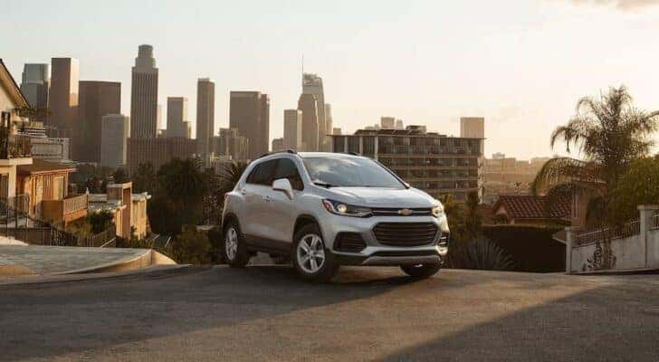A silver 2022 Chevy Trax is shown parked on top of a hill with a city view.