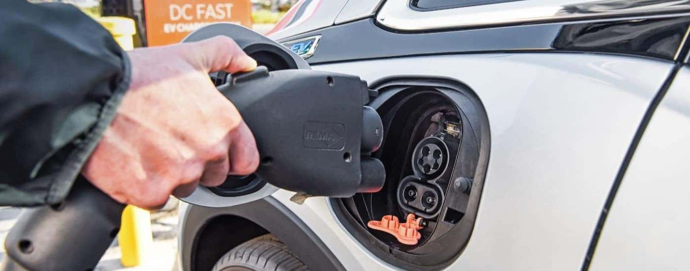 A close up shows a person plugging a charge cable into a silver 2022 Chevy Bolt EV.