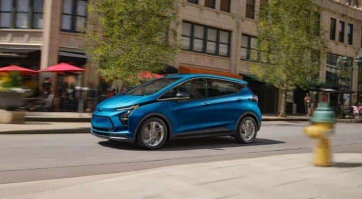 A blue 2023 Chevy Bolt EV for sale is shown driving on a city street.
