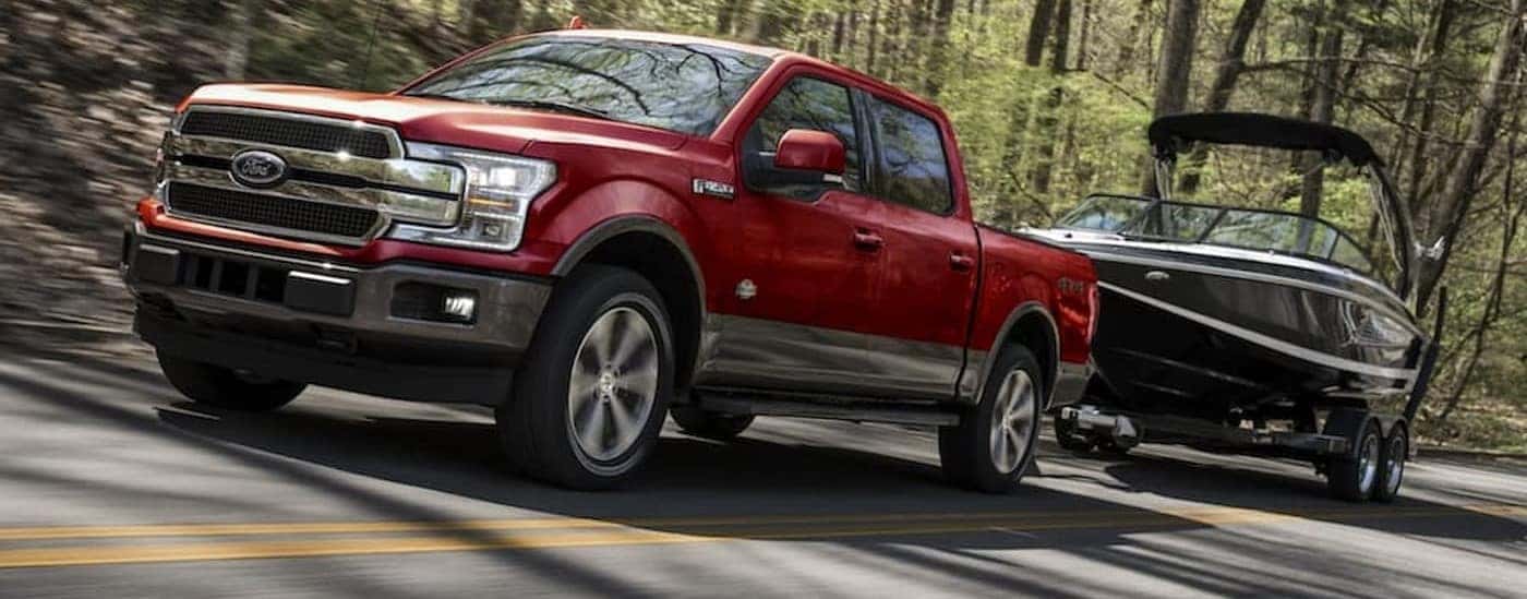 A red 2020 Ford F-150 is shown towing a boat on a highway.