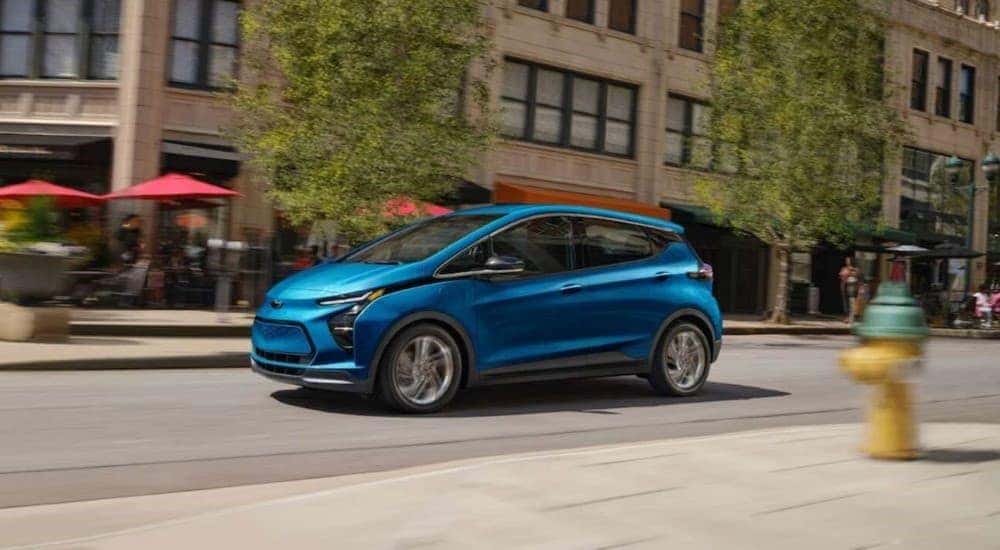 A blue 2023 Chevy Bolt EV is shown driving near city buildings.