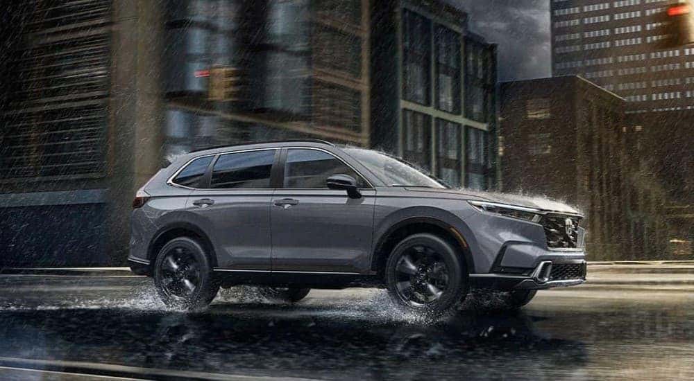 A gray 2024 Honda CR-V Sport Touring is shown driving on a city road.