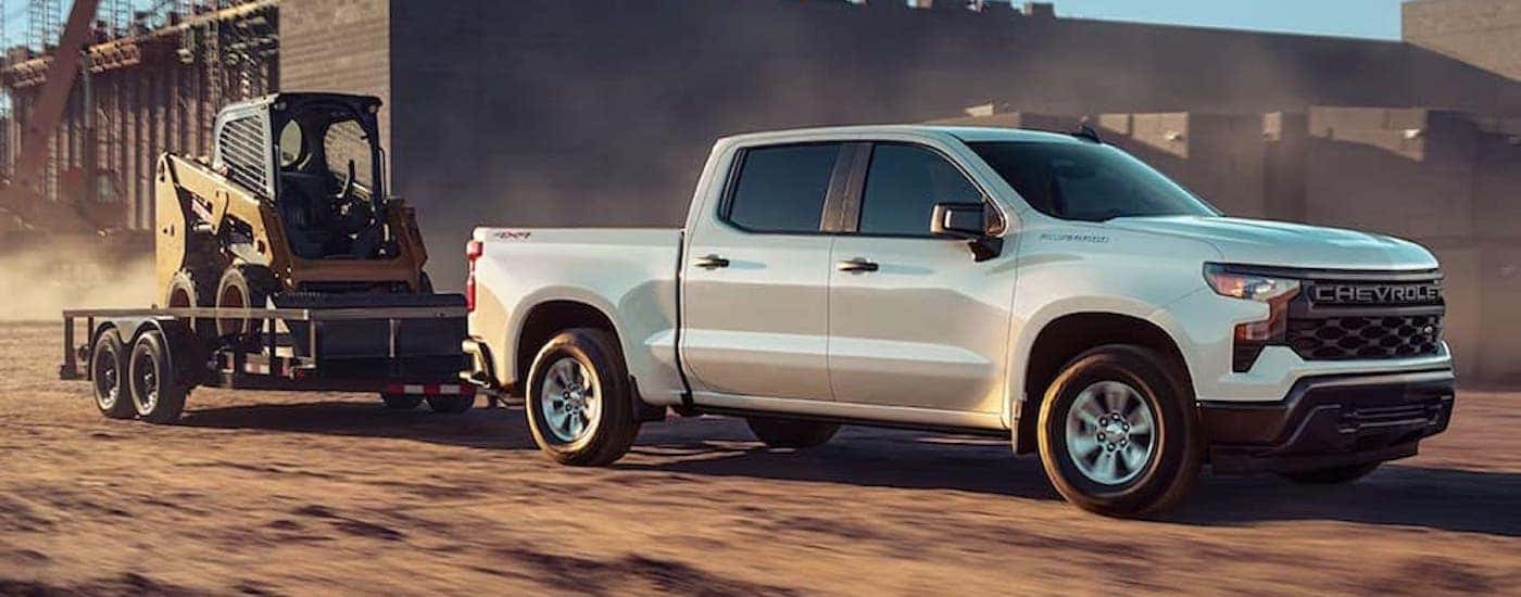 A white 2021 Chevy Silverado 1500 WT is shown from the side while towing a skid-steer.