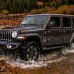 A popular 2018 Jeep Wrangler for sale, a black 2018 Jeep Wrangler Sahara Unlimited, is shown driving off-road.