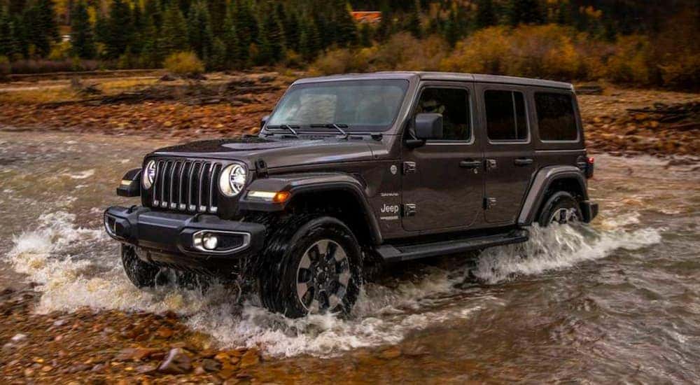 A popular 2018 Jeep Wrangler for sale, a black 2018 Jeep Wrangler Sahara Unlimited, is shown driving off-road.
