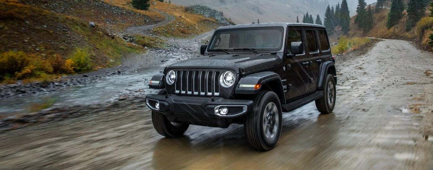 A black 2018 Jeep Wrangler Unlimited is shown driving on a dirt road.