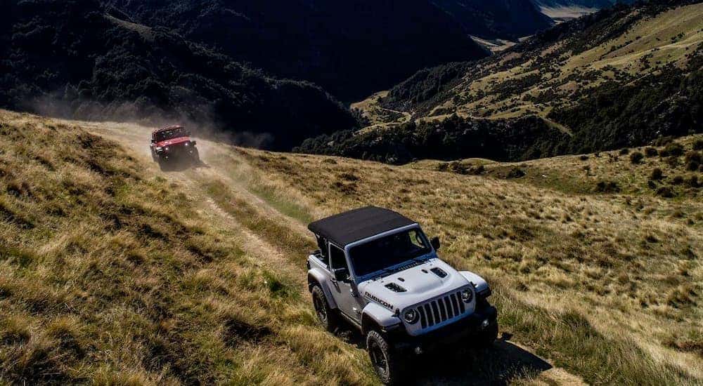A red and white 2018 Jeep Wrangler are shown driving off-road.