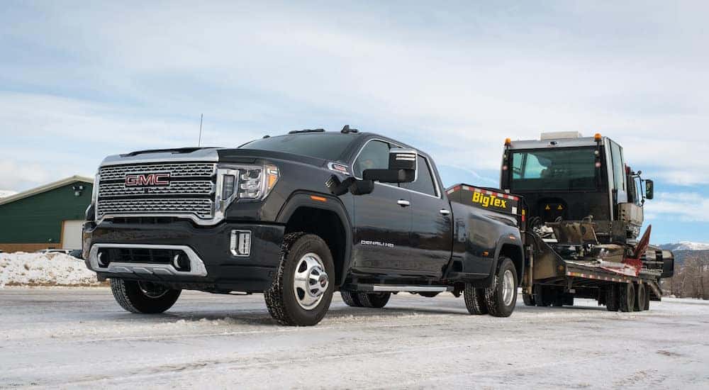 A black 2020 GMC Sierra 3500 HD Denali is shown from the front at an angle while towing heavy equipment.