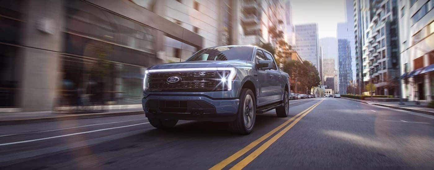 A blue 2023 Ford F-150 Lightning is shown driving on a city street.
