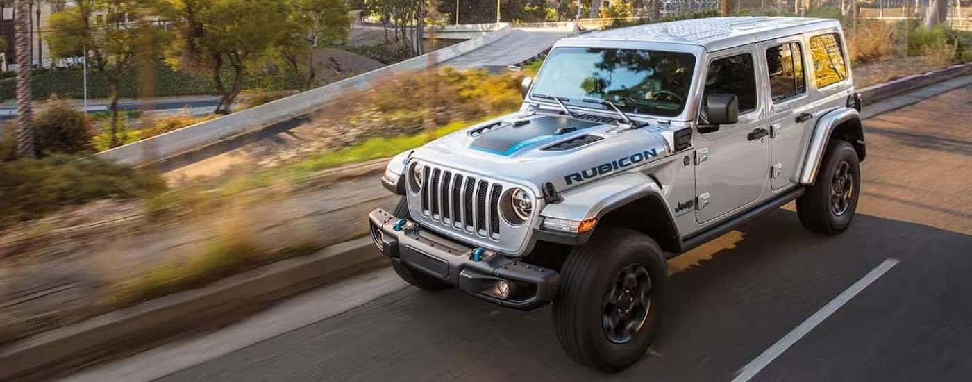 A silver 2023 Jeep Wrangler Rubicon 4xe is shown driving on a city street.