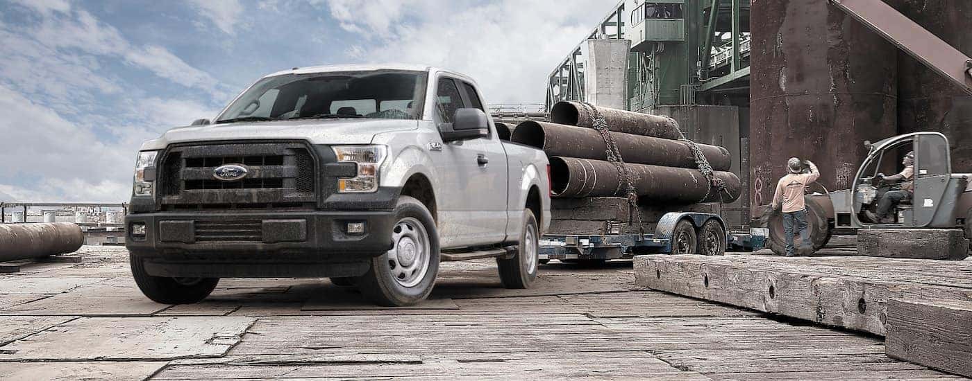 A silver 2015 Ford F-150 is shown towing large pipes.