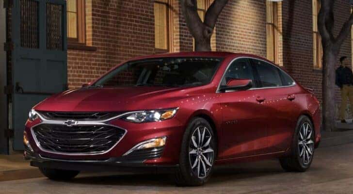A red 2022 Chevy Malibu for sale is shown parked near a brick building.
