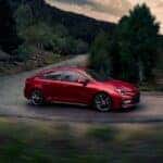 A red 2023 Toyota Corolla is shown from the side while rounding a bend after browsing Dayton car sales.