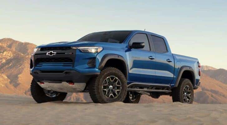 An off-roading Chevy Colorado for sale, a blue 2023 Chevy Colorado ZR2, is shown driving in a desert.