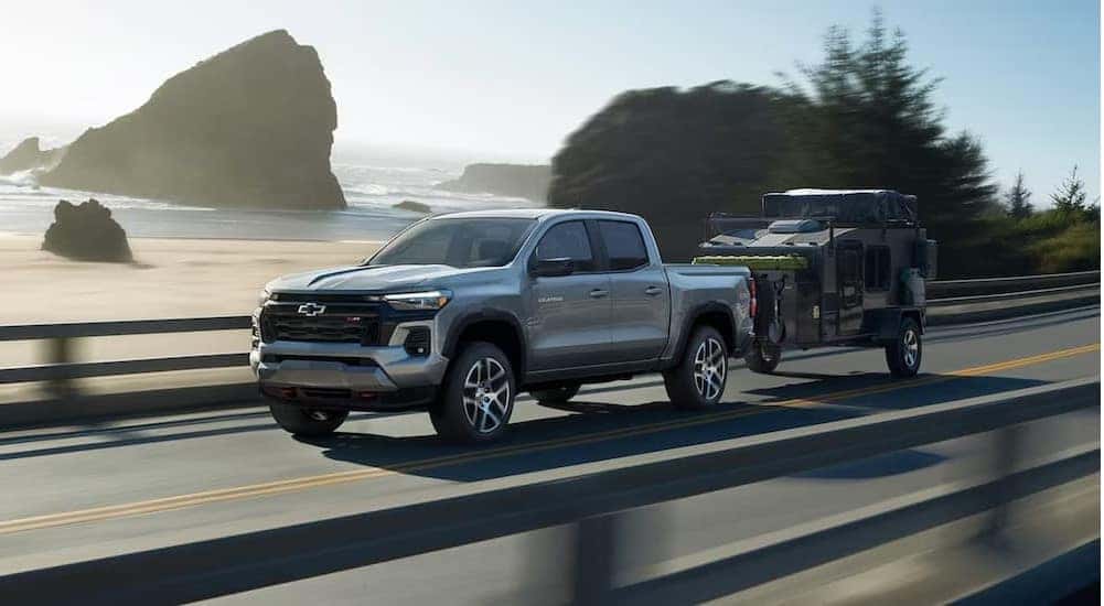 A silver 2024 Chevy Colorado is shown towing a trailer on a highway.