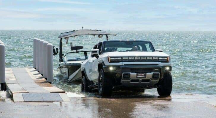 A white 2022 GMC Hummer EV is shown towing a boat.