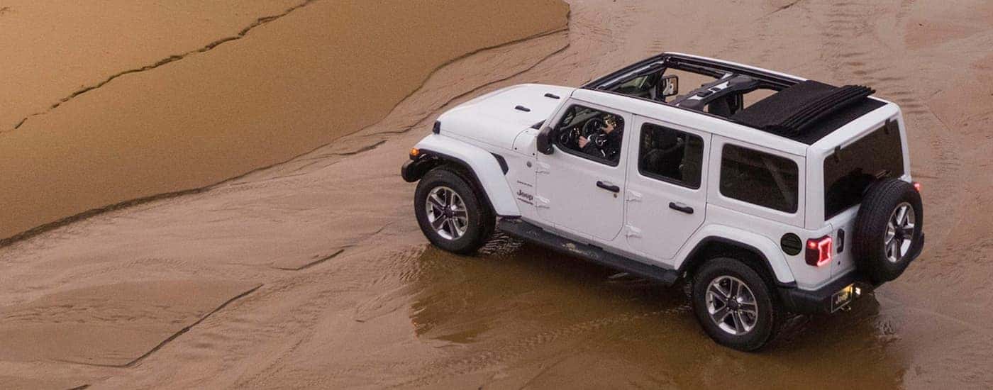 A white 2020 Jeep Wrangler Unlimited is shown from a high angle while driving on a beach.