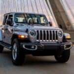 A silver 2021 Jeep Wrangler is shown driving on a bridge after viewing a Jeep Wrangler for sale in Louisville.