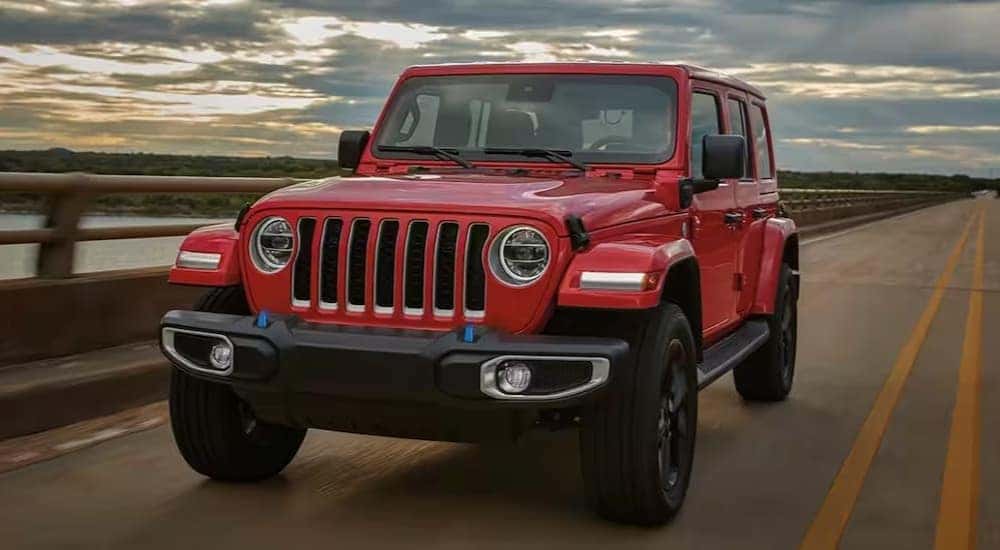 A popular Jeep Wrangler for sale in Cincinnati, a red 2023 Jeep Wrangler, is shown driving on a bridge.