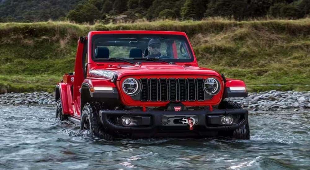 A red 2024 Jeep Wrangler Rubicon is shown driving off-road to view a Jeep Wrangler for sale in Nashville.