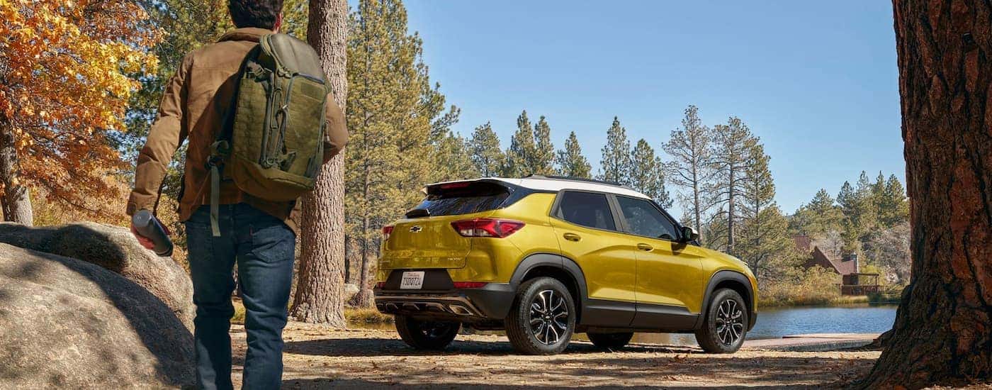 A man is walking towards a yellow 2023 Chevy Trailblazer parked near a hiking area.