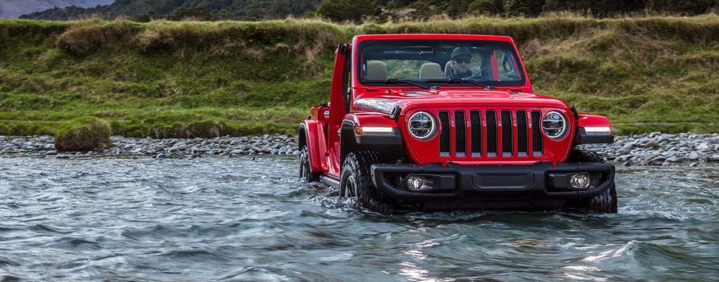 A red 2023 Jeep Wrangler Rubicon is shown fording a river.