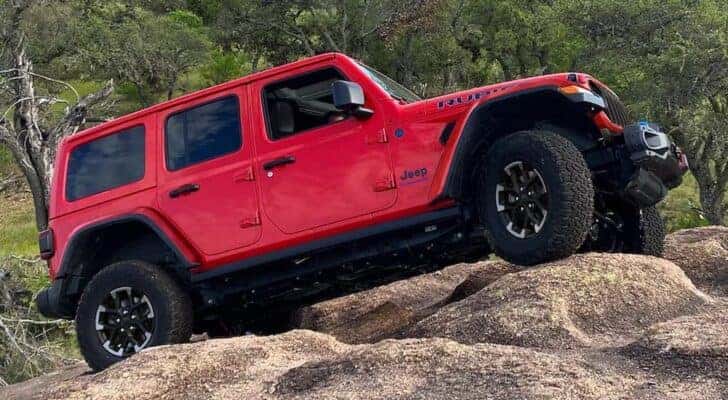 A red 2024 Jeep Wrangler Rubicon is shown at an angle while driving up a rocky outcropping.