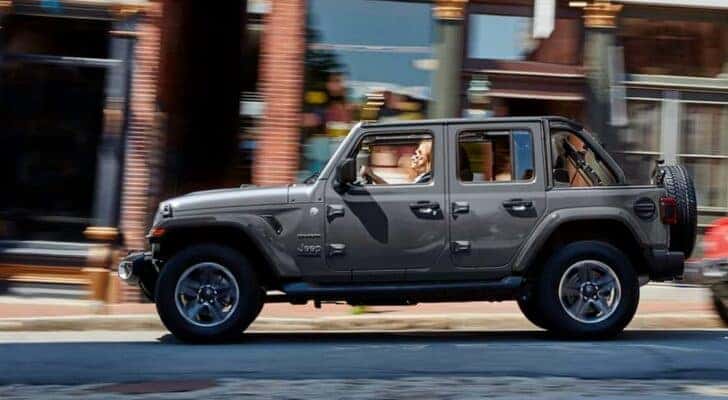 A grey 2021 Jeep Wrangler Sahara Unlimited is shown at a side angle while driving from a dealer with a Jeep Wrangler for sale in Louisville..