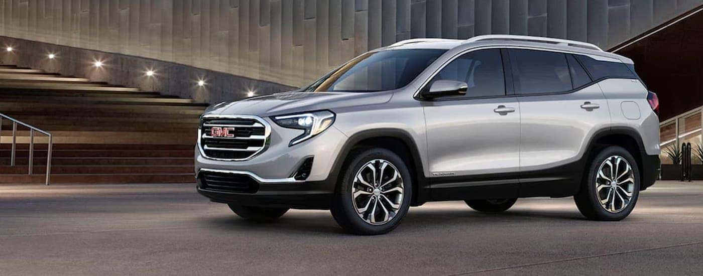 A silver 2020 GMC Terrain for sale angled right and parked outside a building.