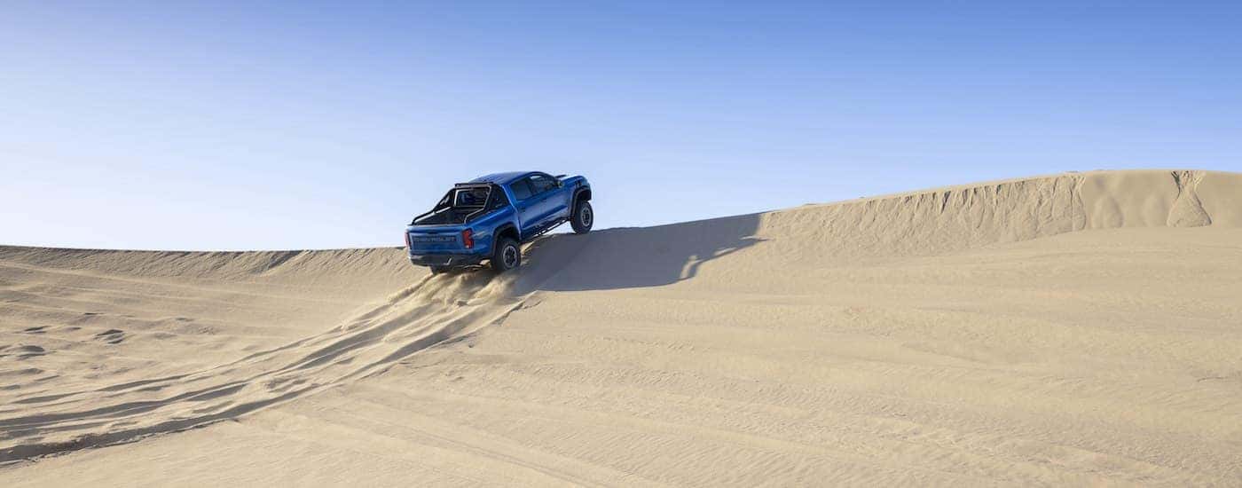 A blue 2023 Chevy Colorado ZR2 is shown from the rear at an angle while jumping off of a sand dune.