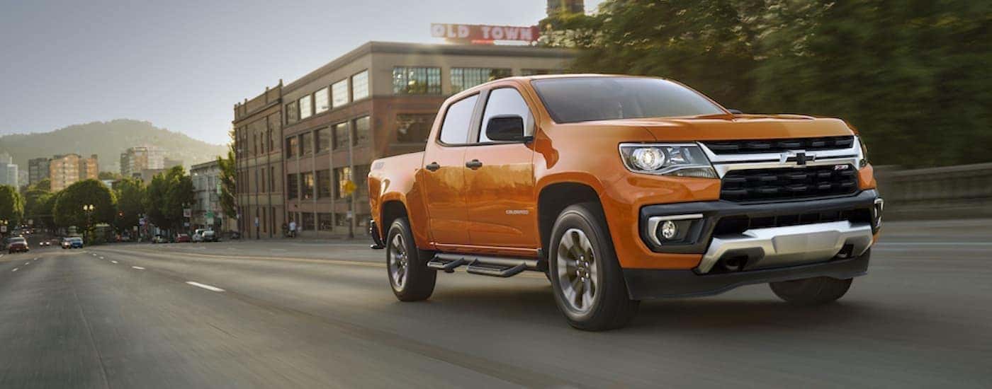 An orange 2021 Chevy Colorado Z71 is driving on a city street.