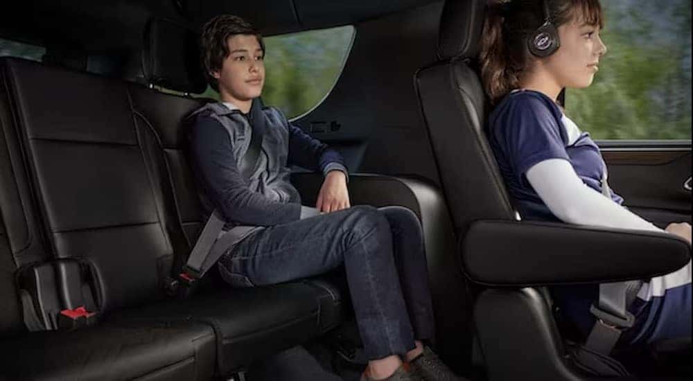 Two children are shown sitting on the black interior seats in a 2023 Chevy Tahoe.