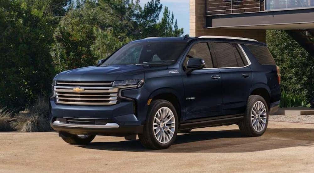 A blue 2024 Chevy Tahoe High Country is shown parked near a house.