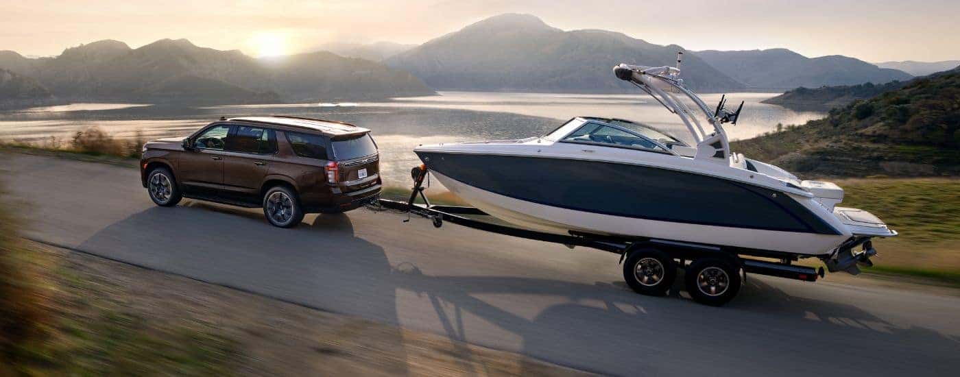 A brown 2022 Chevy Tahoe towing a large boat near water.
