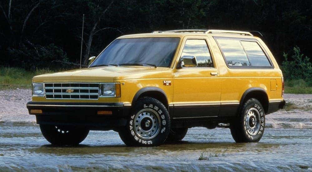 A popular used Chevy Blazer for sale, a yellow 1983 Chevy Blazer S10, is shown parked off-road.