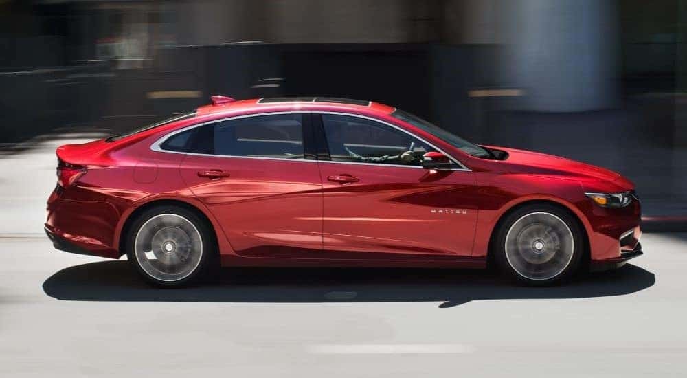 A red 2018 Chevy Malibu is shown driving fast on a city street.