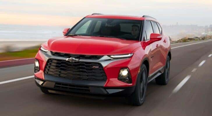 A red 2021 Chevy Blazer RS for sale is driving on a road next to an ocean.