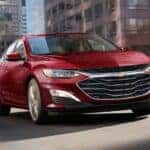 A red 2024 Chevy Malibu for sale in Columbus driving over a bridge.