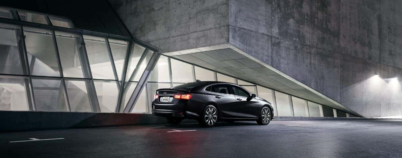A rear view of a black 2024 Chevy Malibu RS Modern parked beside a building.
