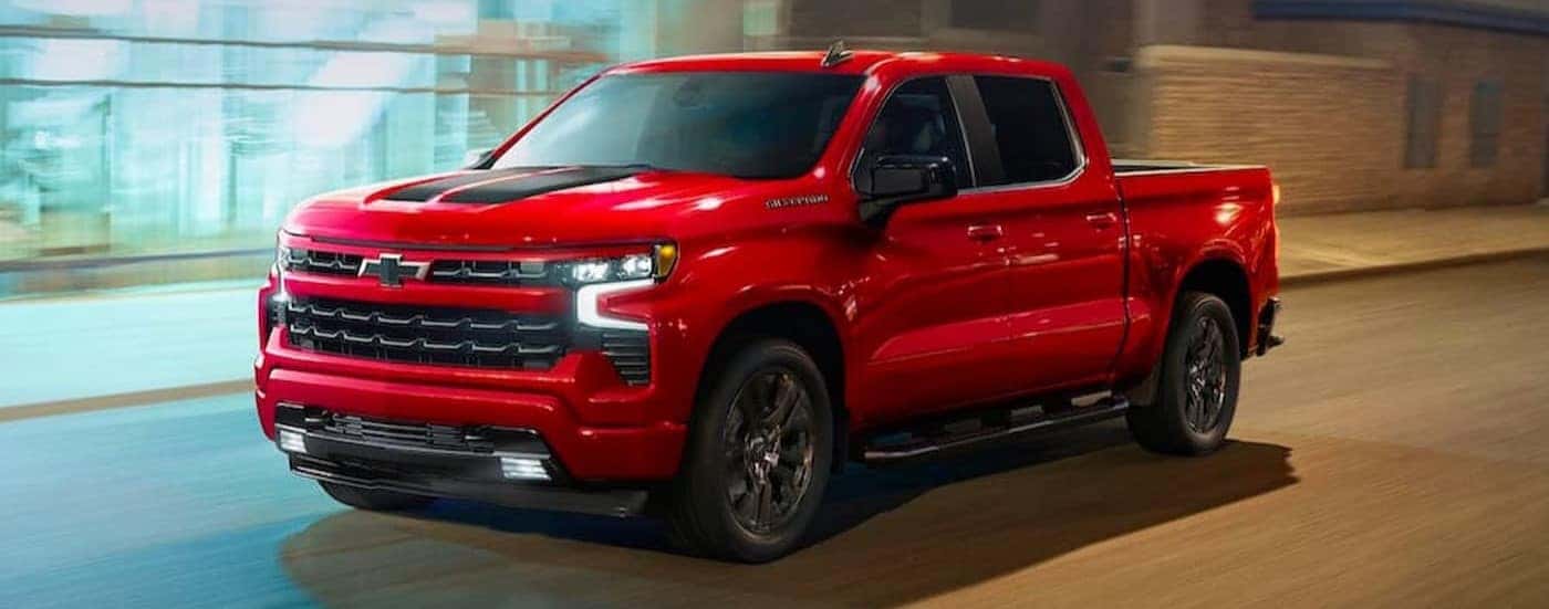A red 2023 Chevy Silverado 1500 RST is shown driving on a city street after viewing a Chevy Silverado for sale.