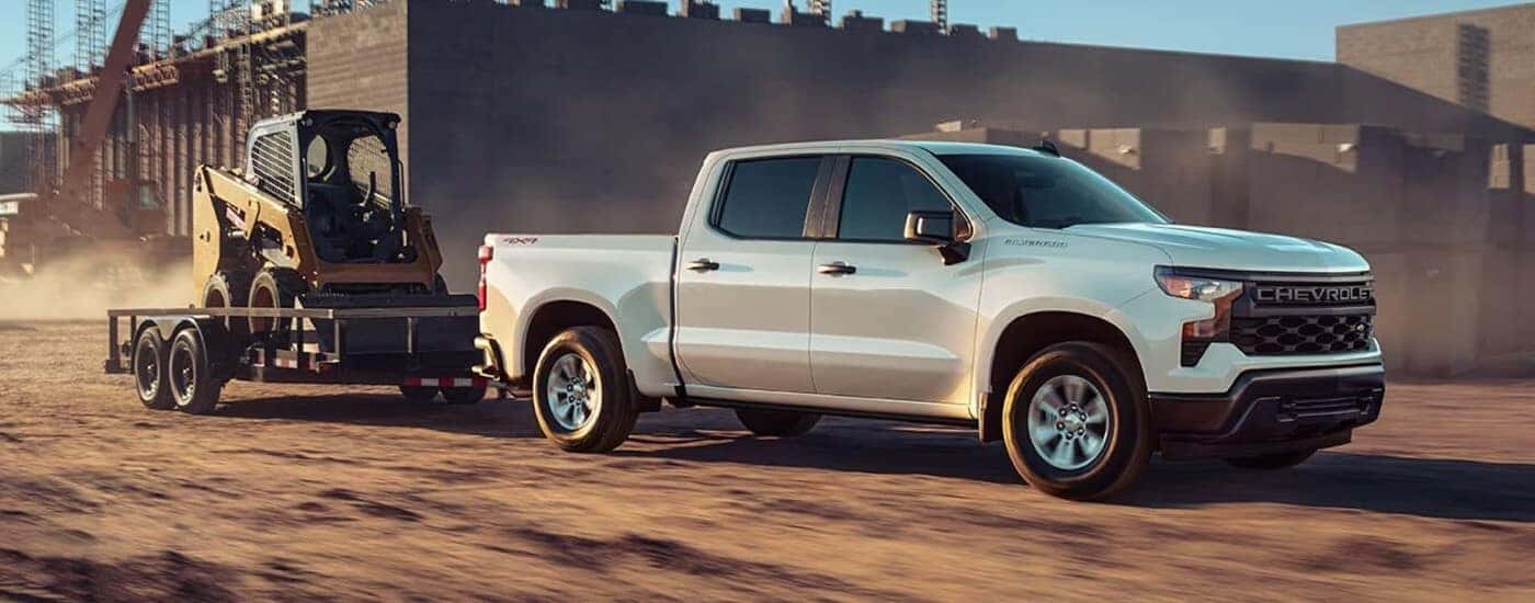 A white 2023 Chevy Silverado 1500 is shown towing a trailer after viewing a Chevy Silverado for sale in Dallas.