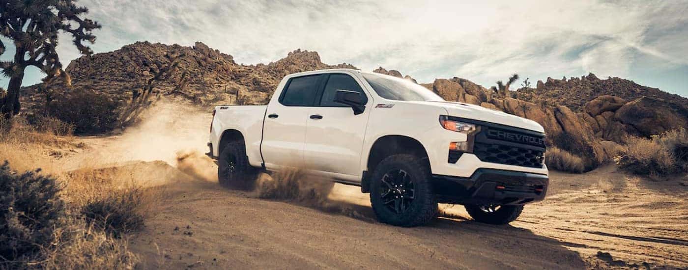 A white 2024 Chevy Silverado 1500 Z71 Custom Trail Boss is shown driving off-road.