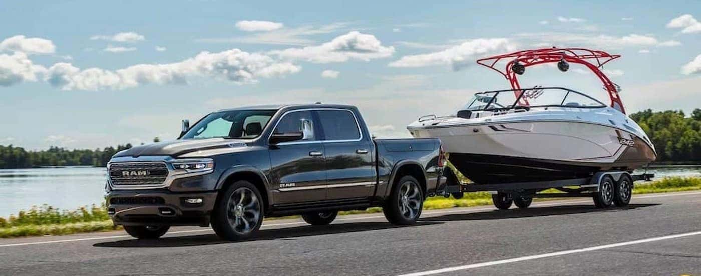 A gray 2024 Ram 1500 is shown towing a boat near a lake.