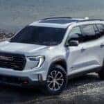 A white 2024 GMC Acadia AT4 is shown parked near a lake.